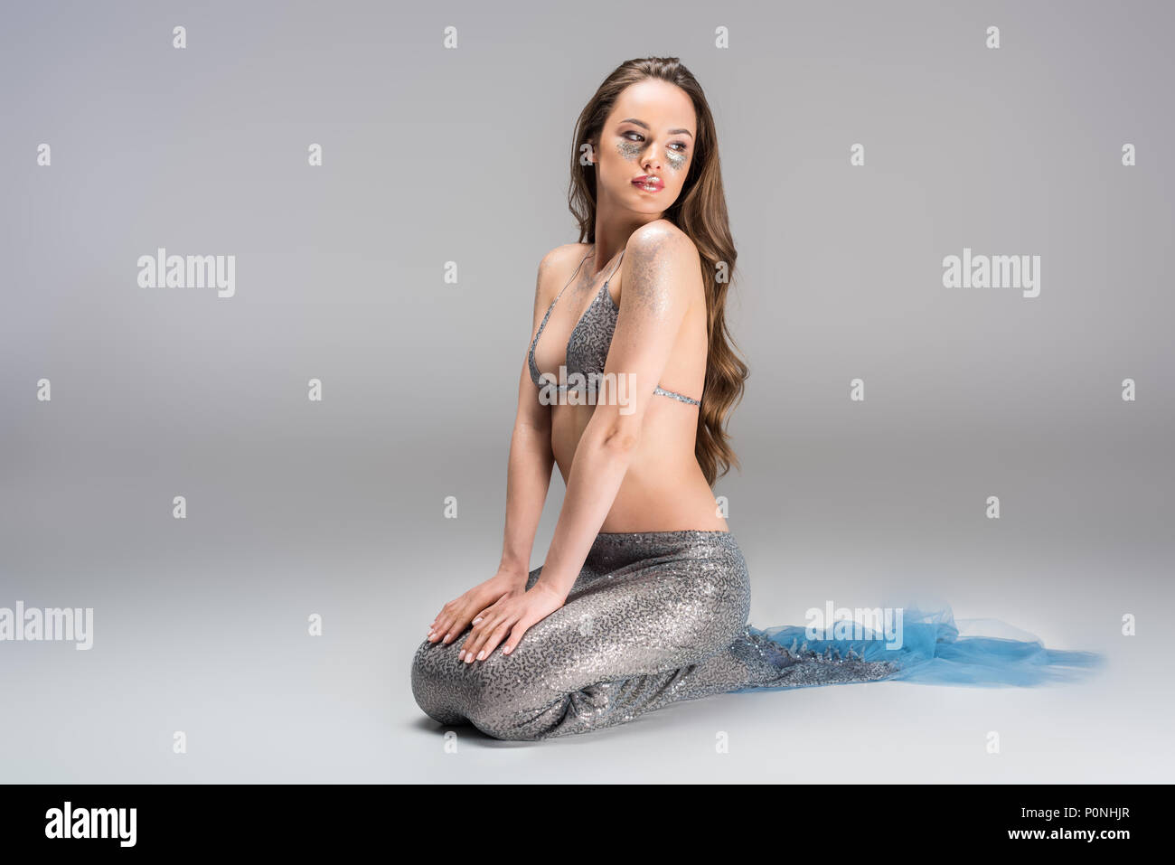 attractive woman with mermaid tail and silver top sitting on floor Stock Photo