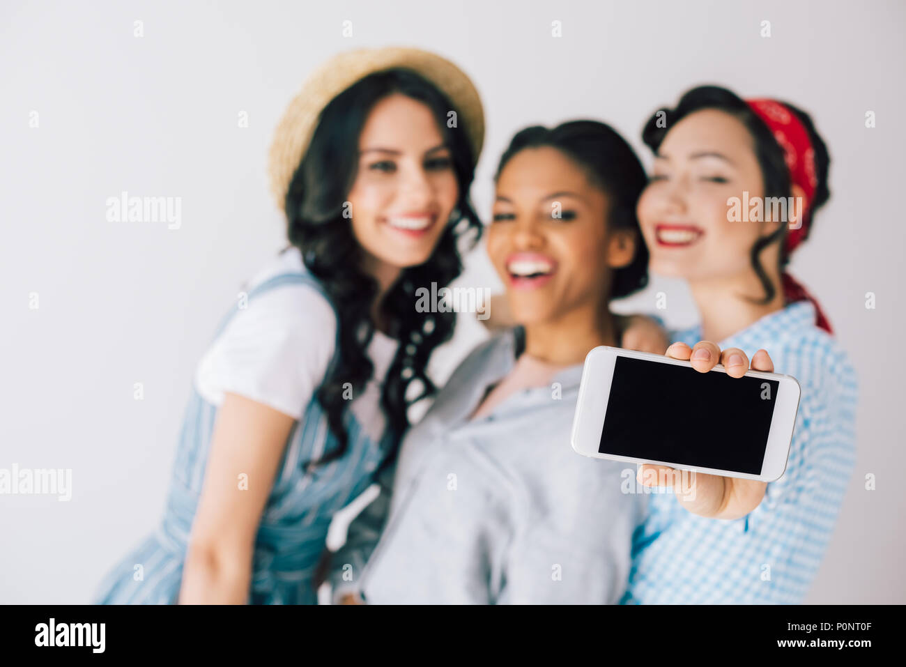 selective focus of multicultural happy women taking selfie on smartphone together isolated on grey Stock Photo