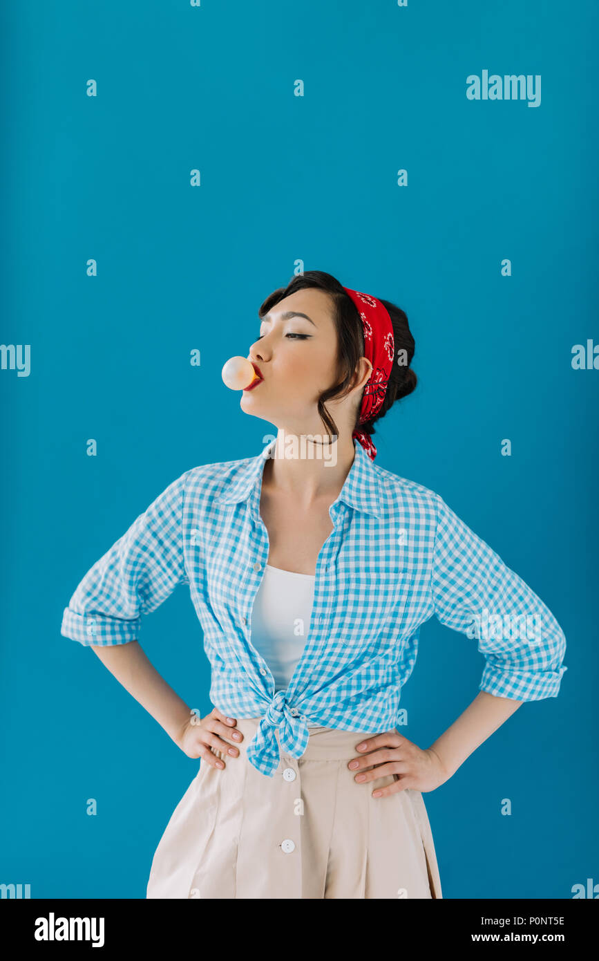 portrait of asian woman in retro clothing standing akimbo and blowing  bubble gum isolated on blue Stock Photo - Alamy