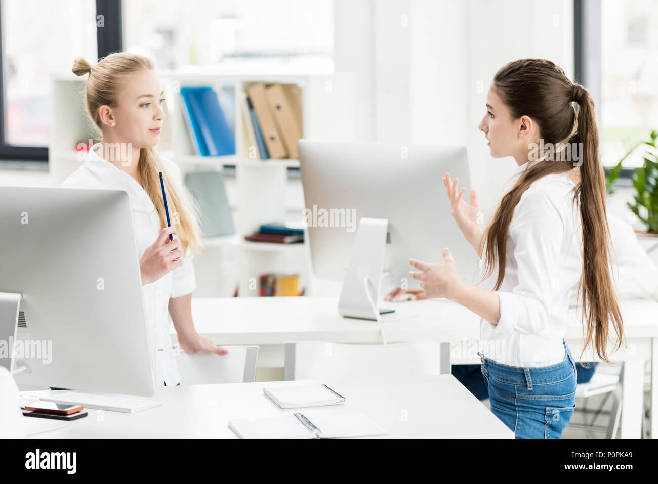 side view of teen girls discussing task together while standing in computer class Stock Photo