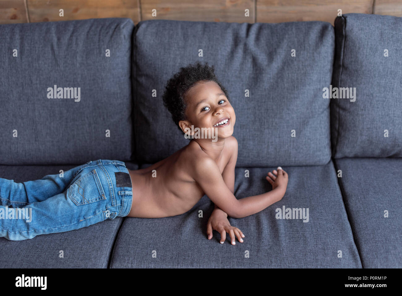 shirtless little smiling africanamerican kid playing on sofa Stock