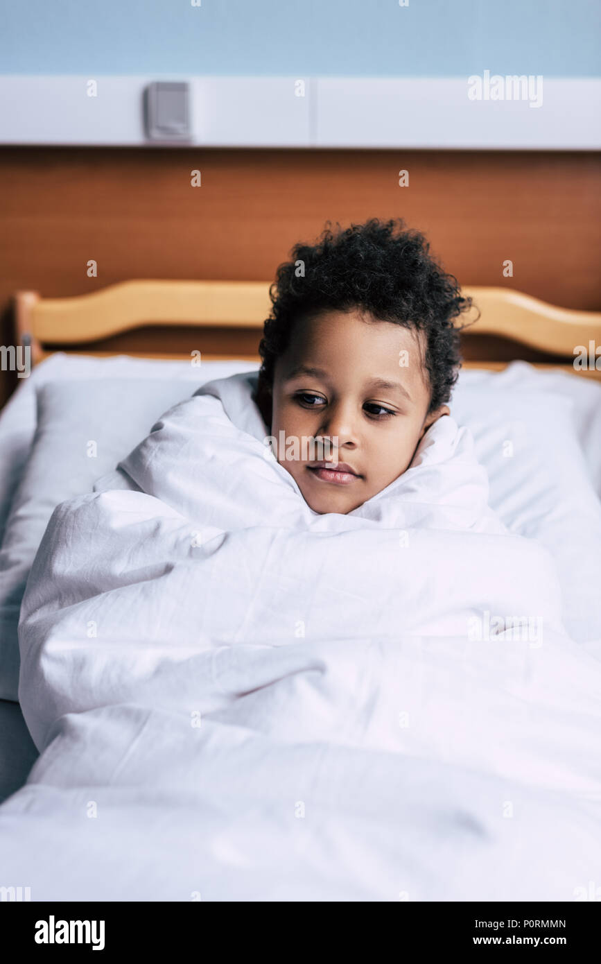 portrait of pensive african american boy in blanket looking away while  resting on bed Stock Photo - Alamy