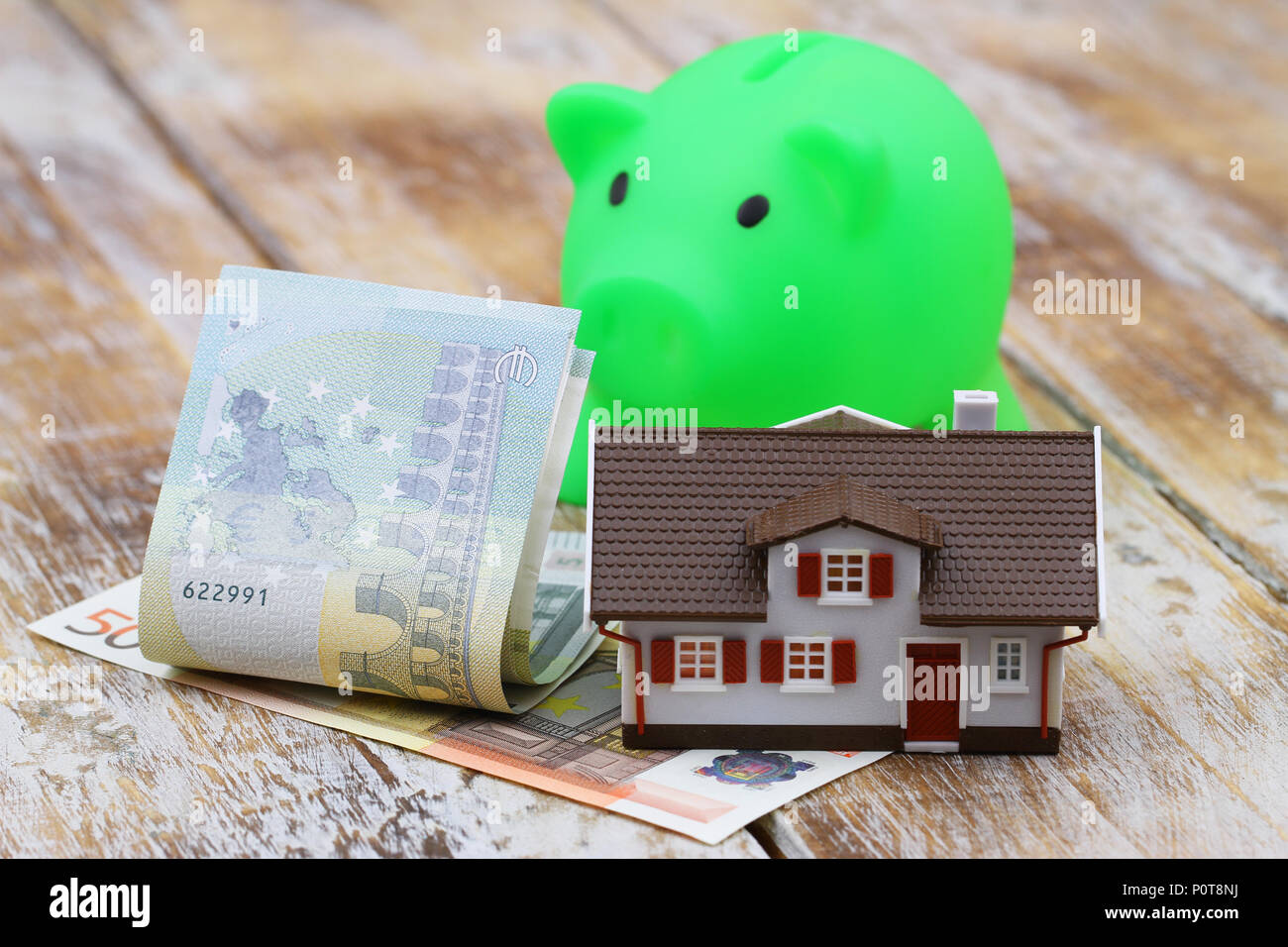 Model of a house, EUR banknotes and piggy bank on wooden surface Stock Photo