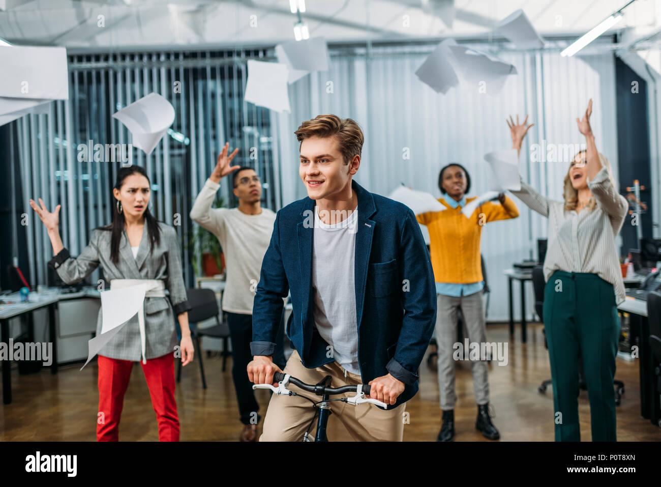 young businessman riding bike at office while partners throwing up