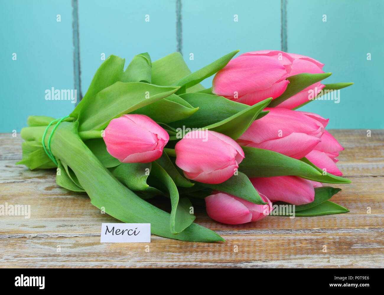 Merci (thank you in French) card with pink tulip bouquet on rustic wooden surface Stock Photo