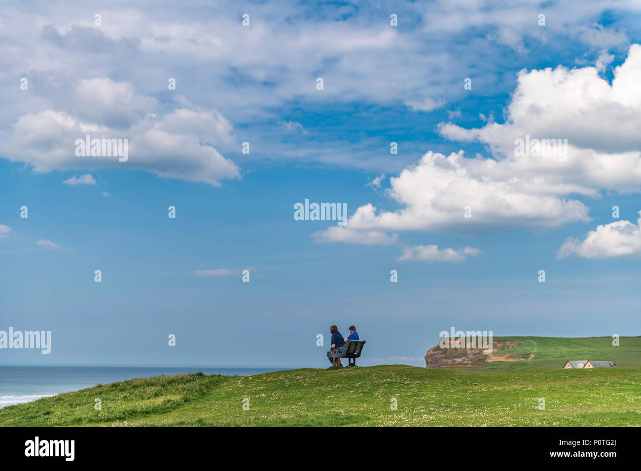 A couple sit on a bench and enjoy the panoramic view over the North Cornwall holiday resort of Bude. Stock Photo