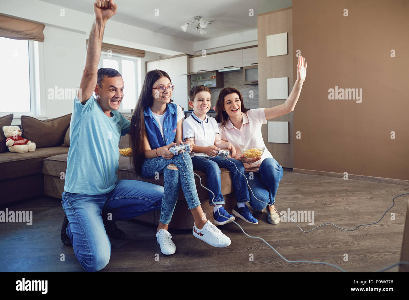 A cheerful family is playing video games while sitting on a sofa in the house. Stock Photo