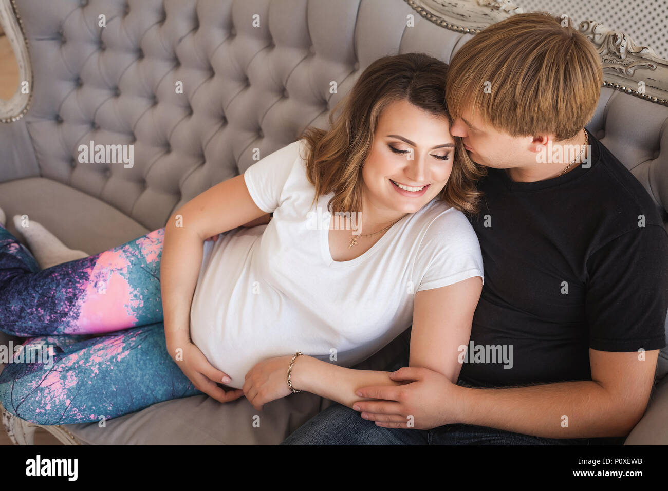 Young attractive couple, future parents hugging on sofa in studio Stock Photo