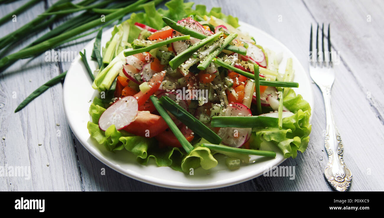 Spring Vegetable Salad on the white plate. Radish, tomato, celery and cucumber. Topped with sesame seeds. Vegetarian dish on the white wooden table. C Stock Photo
