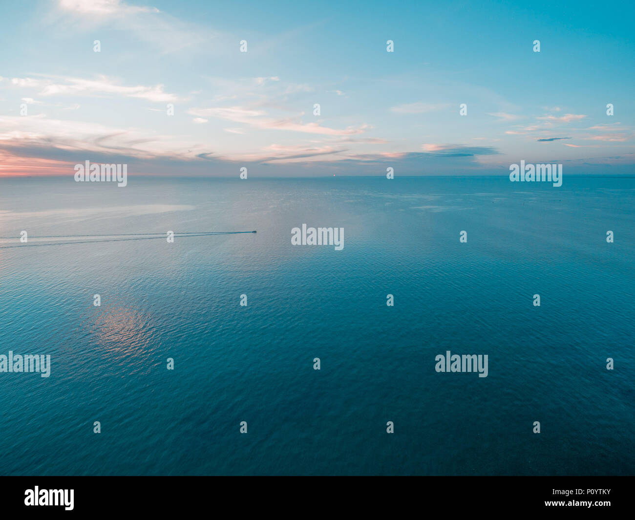 Tiny fishing boat sailing across calm sea at dusk Stock Photo - Alamy