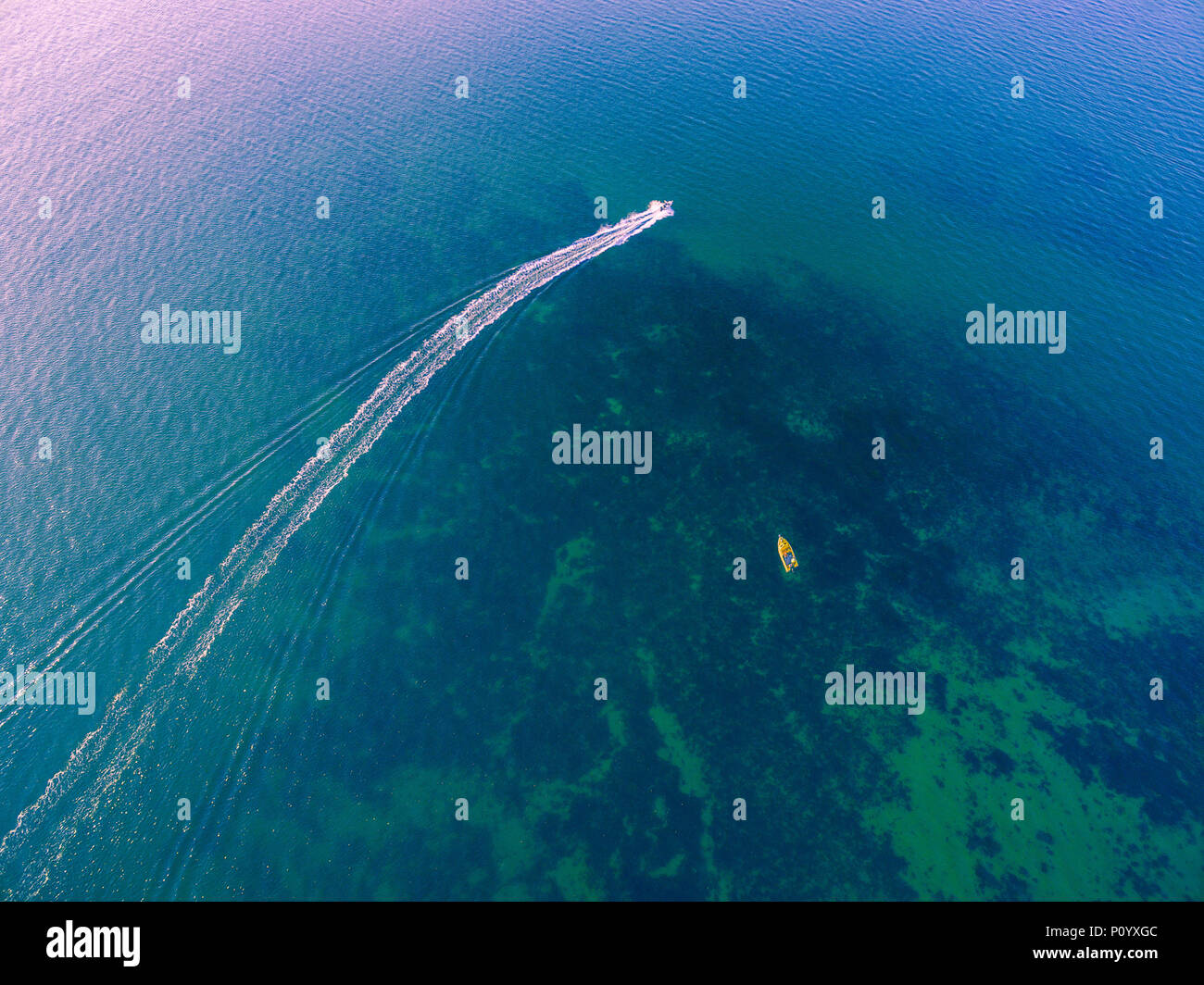 Aerial view of small sailing fishing boat leaving white water trail on shallow ocean water Stock Photo