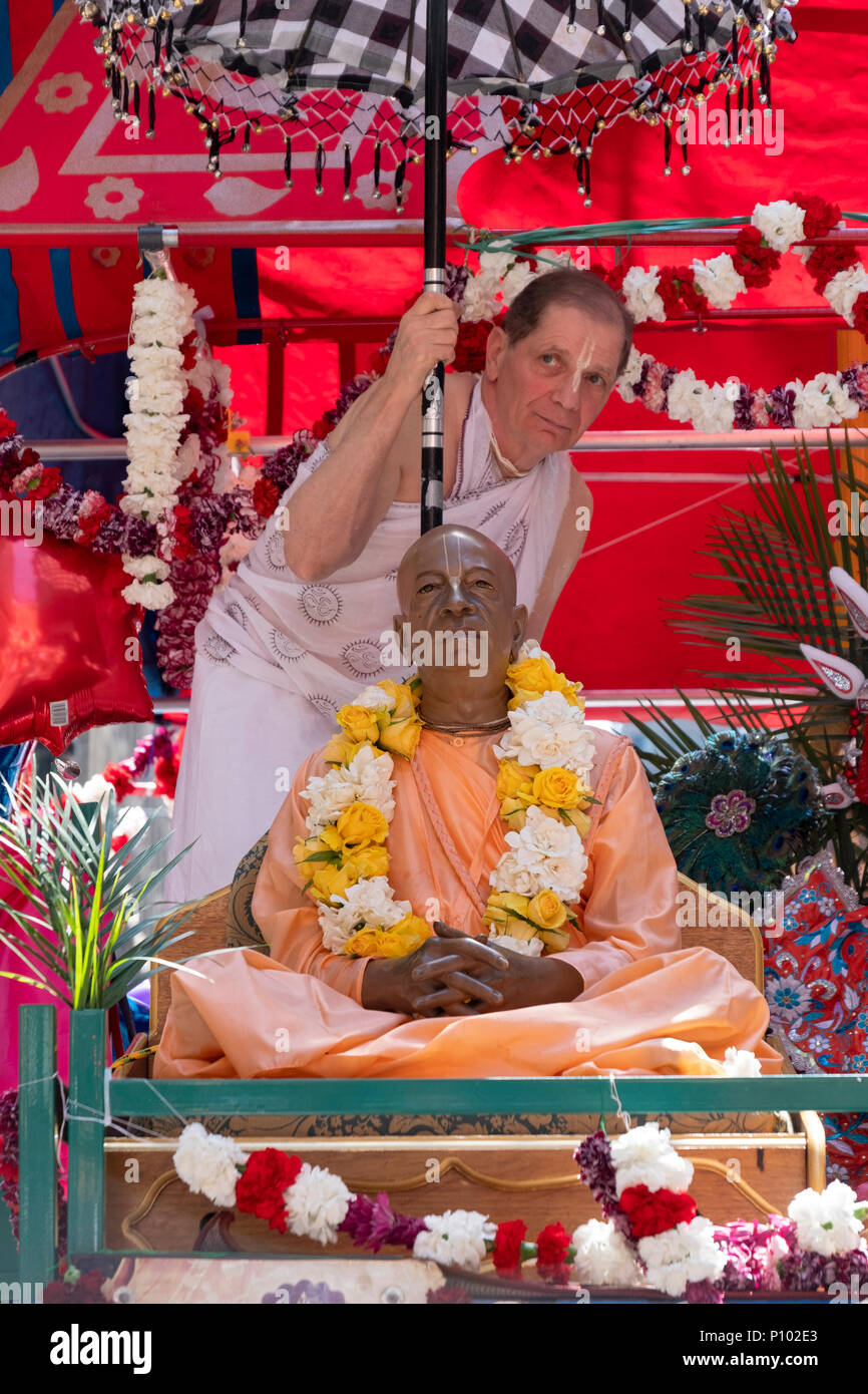 A man in a white sari holding an umbrella over a statue of the founder of the Hare krishna movement at the Rathayatra festival in Midtown Manhattan. Stock Photo