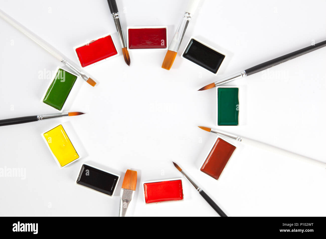 Solid watercolors pans with various paint brushes arranged in circle with copy space on white background Stock Photo