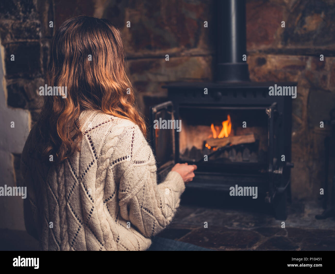 A young woman is poking a fire in a log burner Stock Photo