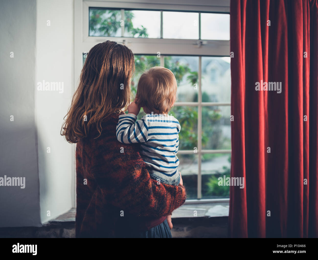 A young wmother is looking out the window with her little toddler boy Stock Photo