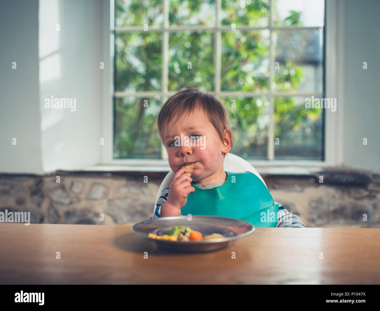 A cute little boy is sitting at the table and is eating his dinner