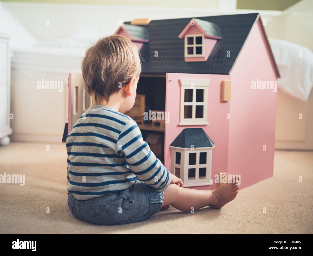 A cute gender confident little boy is busting stereotypes and socially imposed expectations by playing with a big pink doll house and having a great t Stock Photo