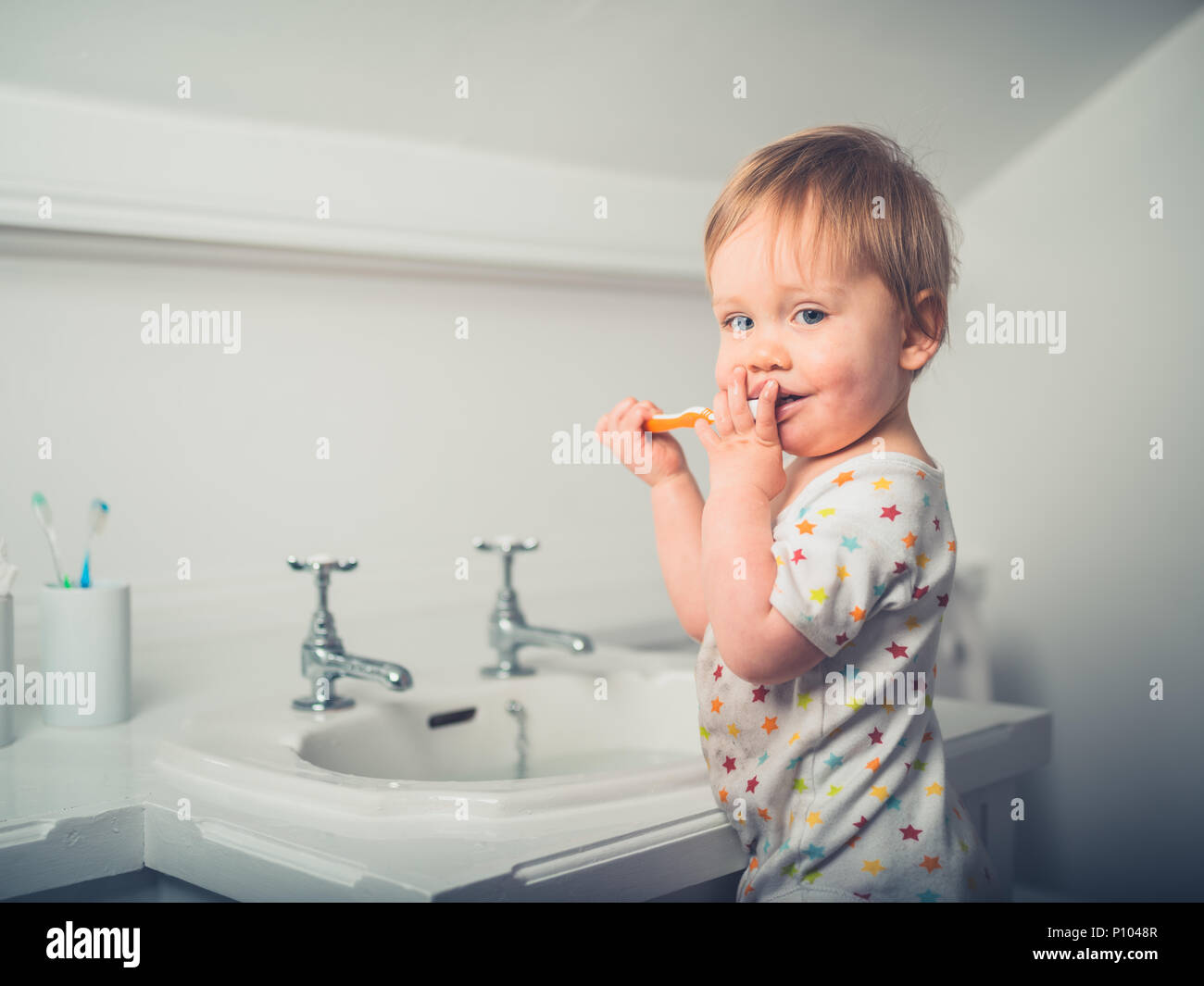 A cute little boy is brushing his teeth by the sink in a bathroom Stock Photo