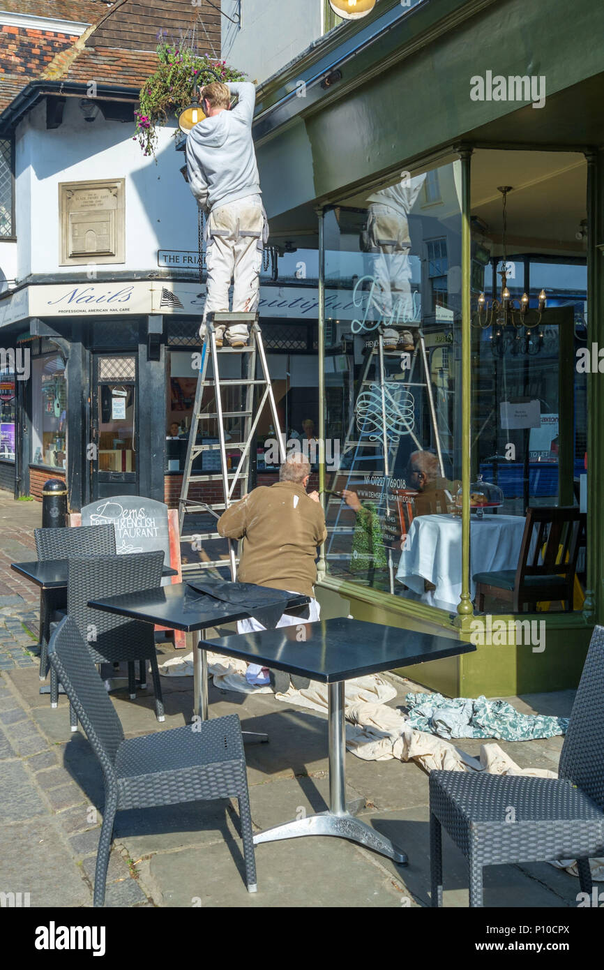 Workmen using a ladder to work on a shop front in Canterbury, Kent, England, UK. Stock Photo