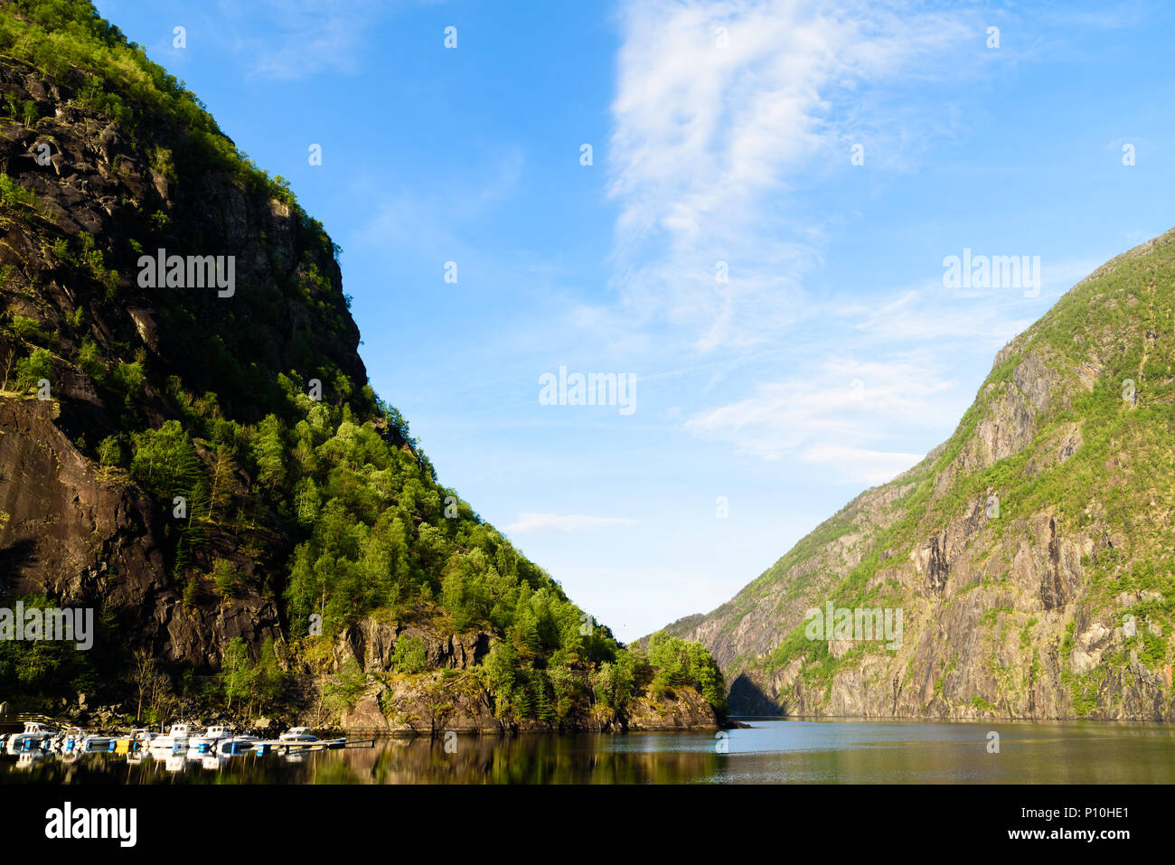 The fjord Akrafjorden on a sunny morning. High mountains on both sides and a marina just below a steep cliff. Location Fjaera in Hordaland, Norway. Stock Photo