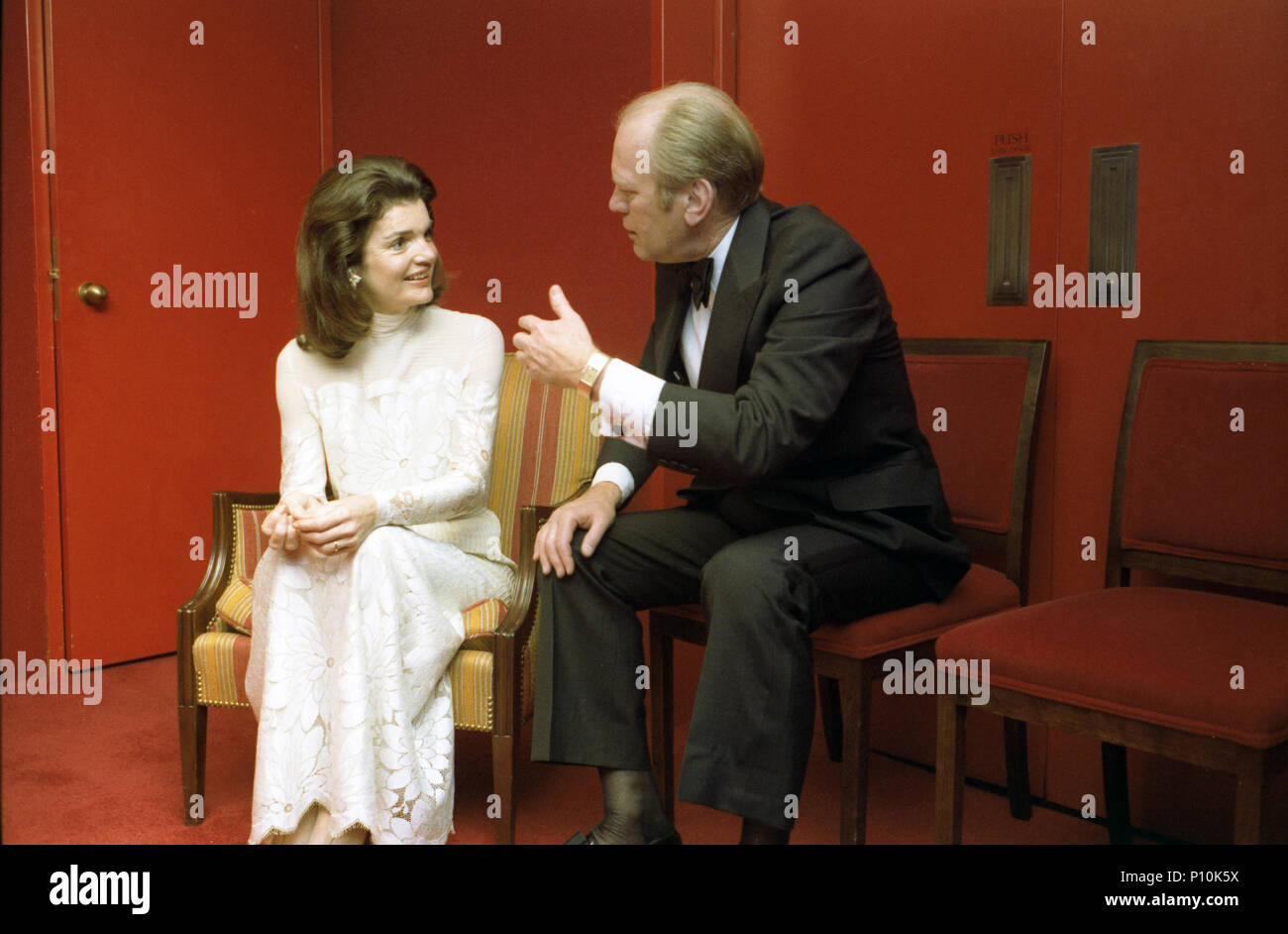1976, January 25 – John F. Kennedy Center for the Performing Arts - African Room –  Gerald R. Ford, Jacqueline Bouvier Kennedy Onassis – seated, talking; formal wear – Bicentennial Salute to the Performing Arts - Intermission Reception; First Ladies Stock Photo