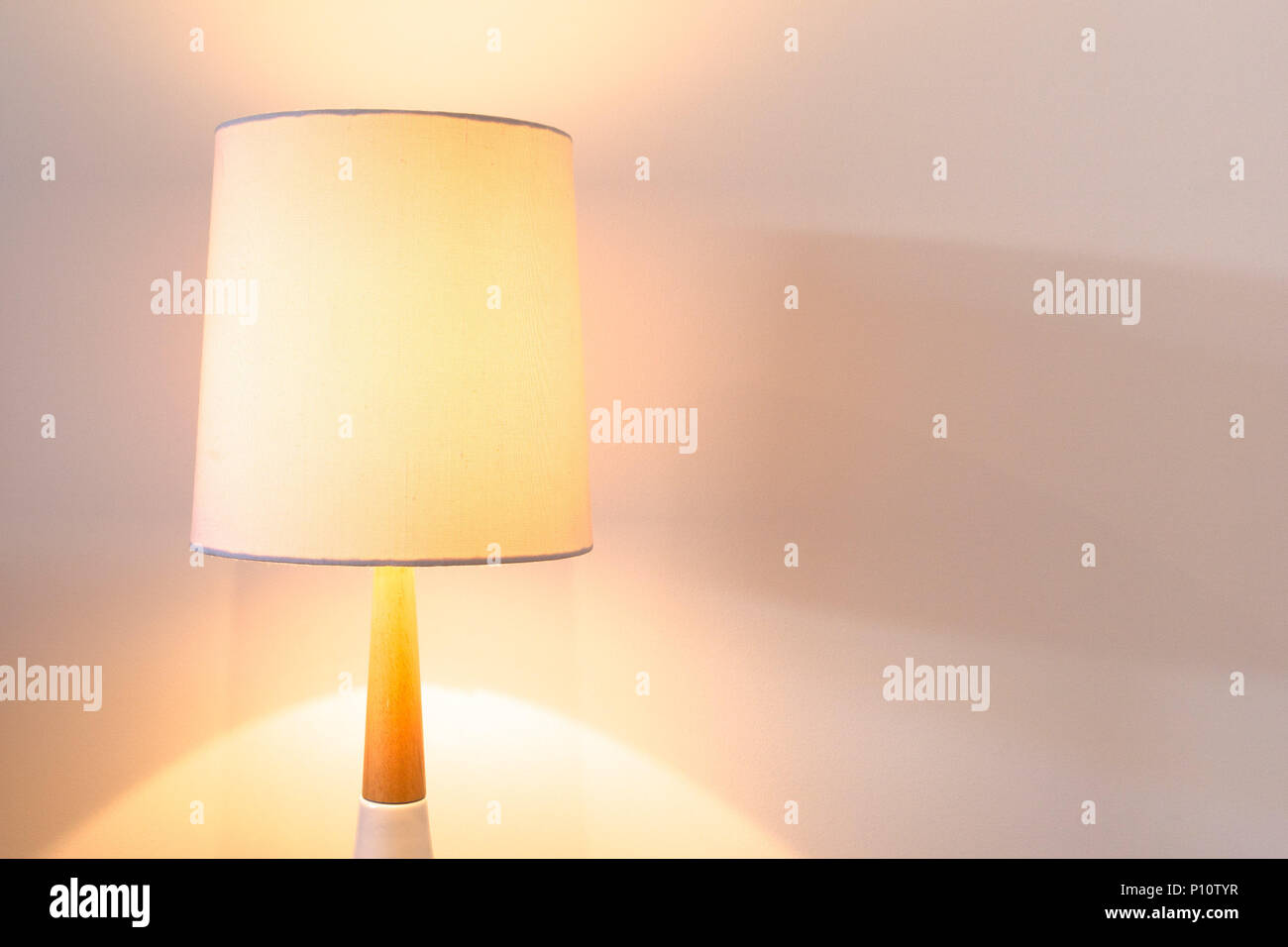 Bedroom lamp with white lampshade lit against white wall with copy