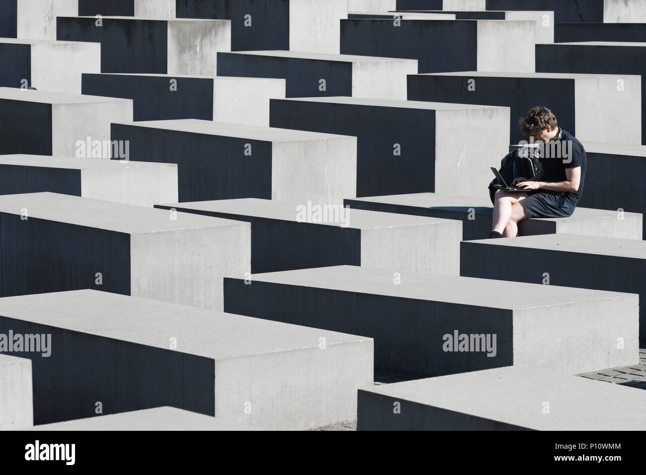 White man is typing on laptop and sitting on a block of Holocaust Memorial, Berlin, Germany Stock Photo