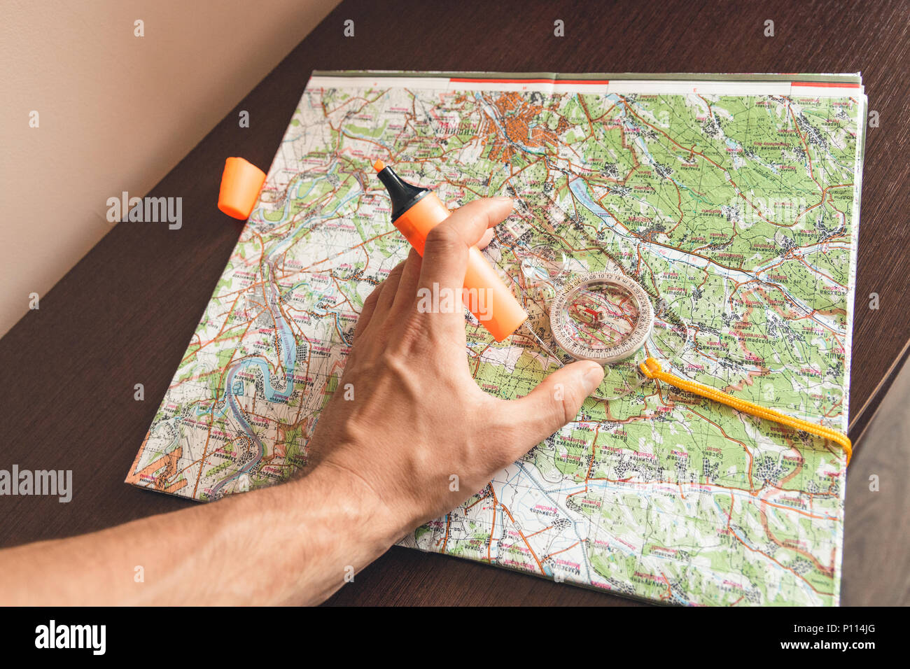 Man holding an orange marker above a map looking for a path Stock Photo