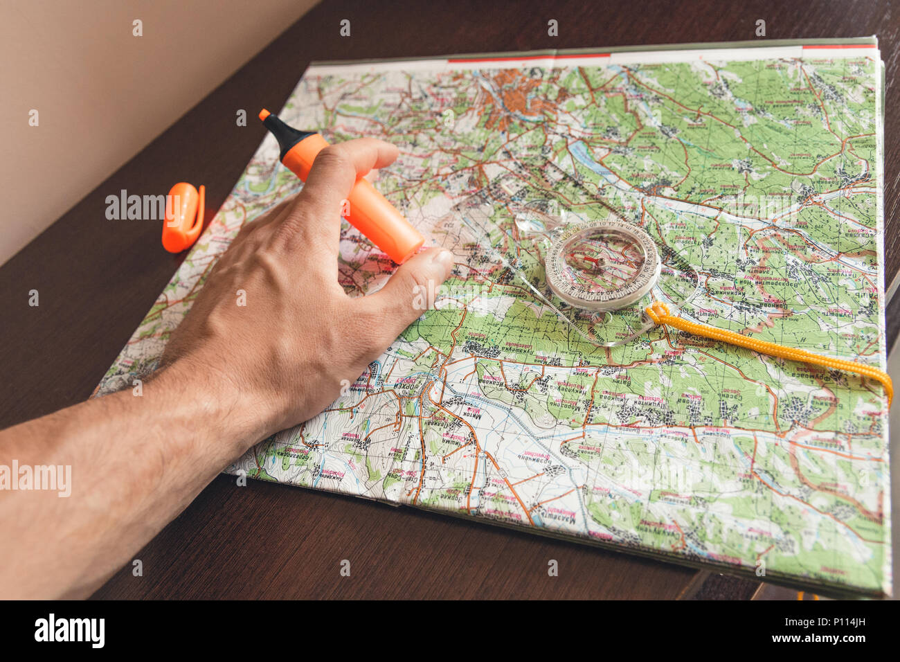 Man holding an orange marker above a map looking for a path Stock Photo
