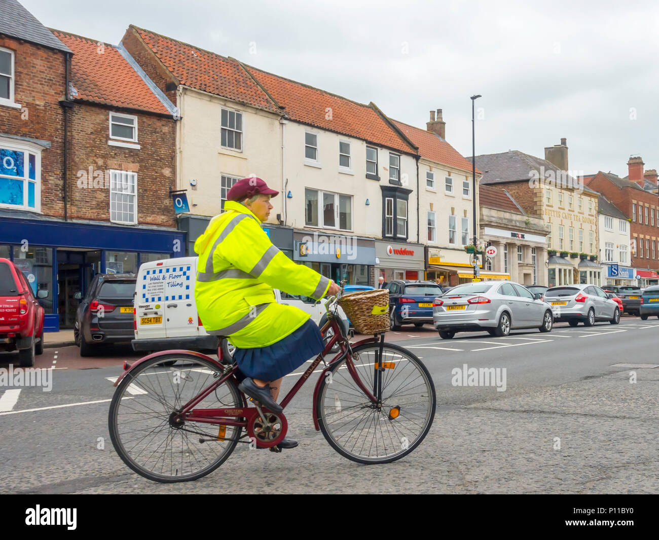 A middle aged woman wearing a high visibility jacket riding a utility bicycle in traffic in busy Northallerton High Street North Yorkshire Stock Photo
