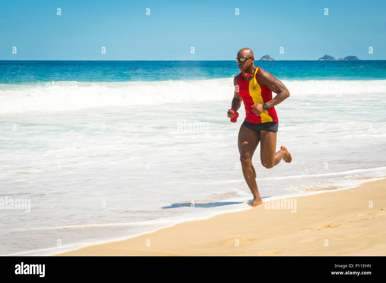 RIO DE JANEIRO - CIRCA MARCH, 2014: Brazilian lifeguard in uniform running along the shore of Ipanema Beach. Slow shutter speed and motion blur Stock Photo