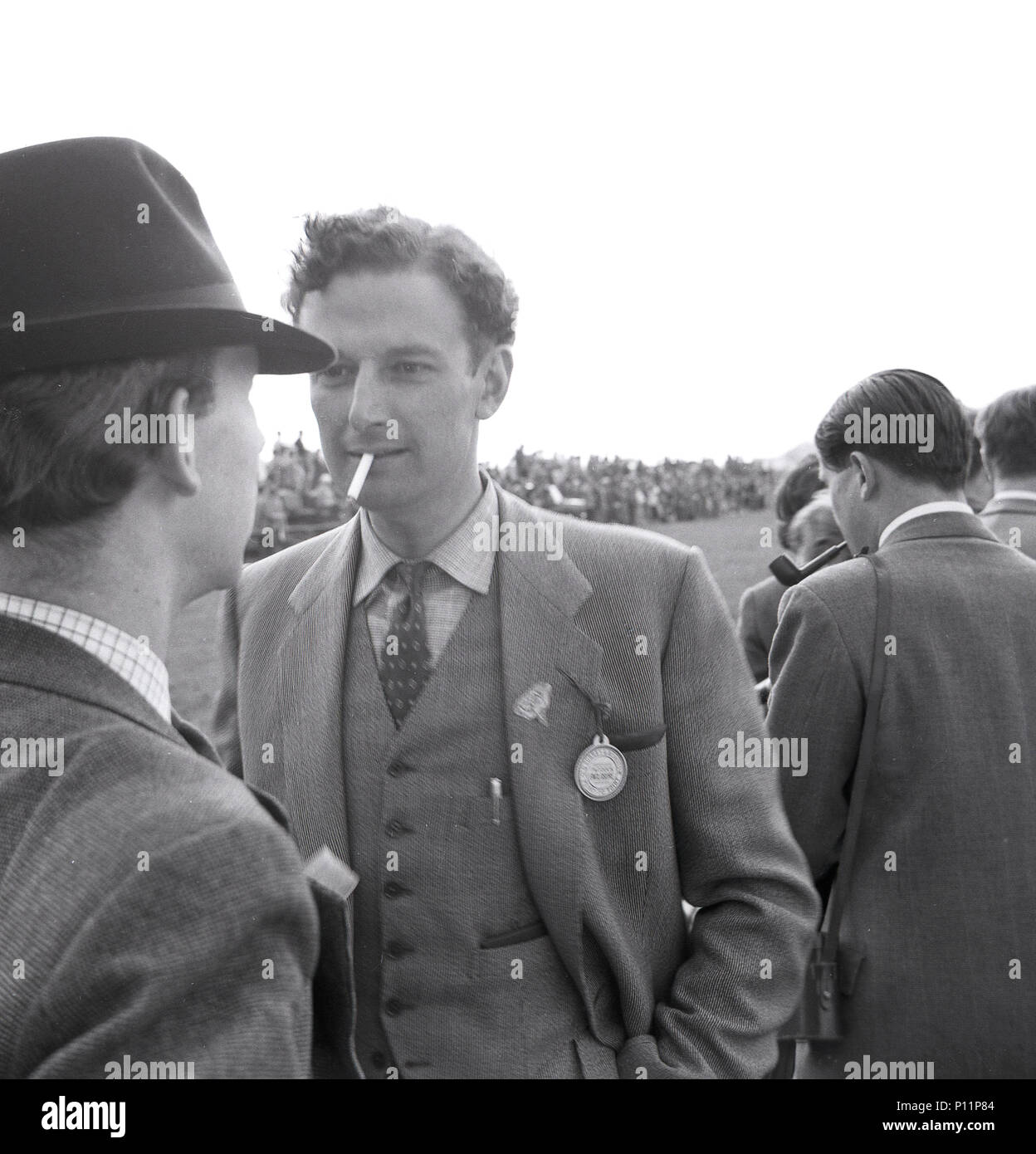 1958, May, well-dressed male race goers - one smoking a cigarette, the another a pipe - outside at a point-to-point amateur horse race meeting at Penshurst, Edenbridge, England, UK. Stock Photo