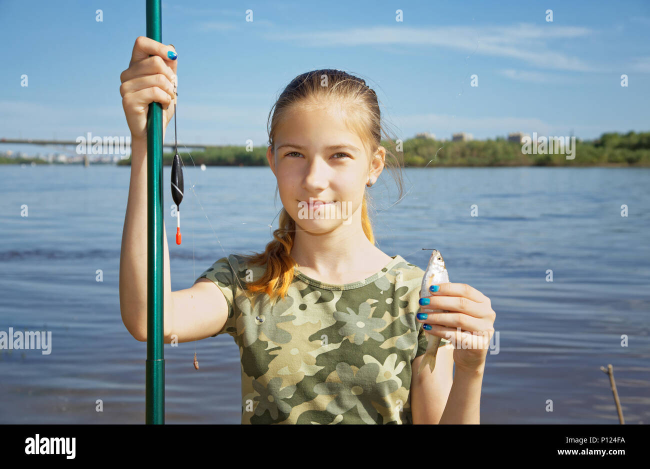 Happy teen girl holding a fishing rod and catch - a small fish