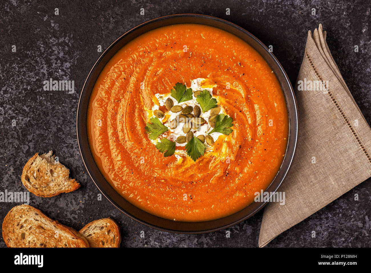 Pumpkin and carrot soup with cream, seeds and parsley. Top view. Stock Photo