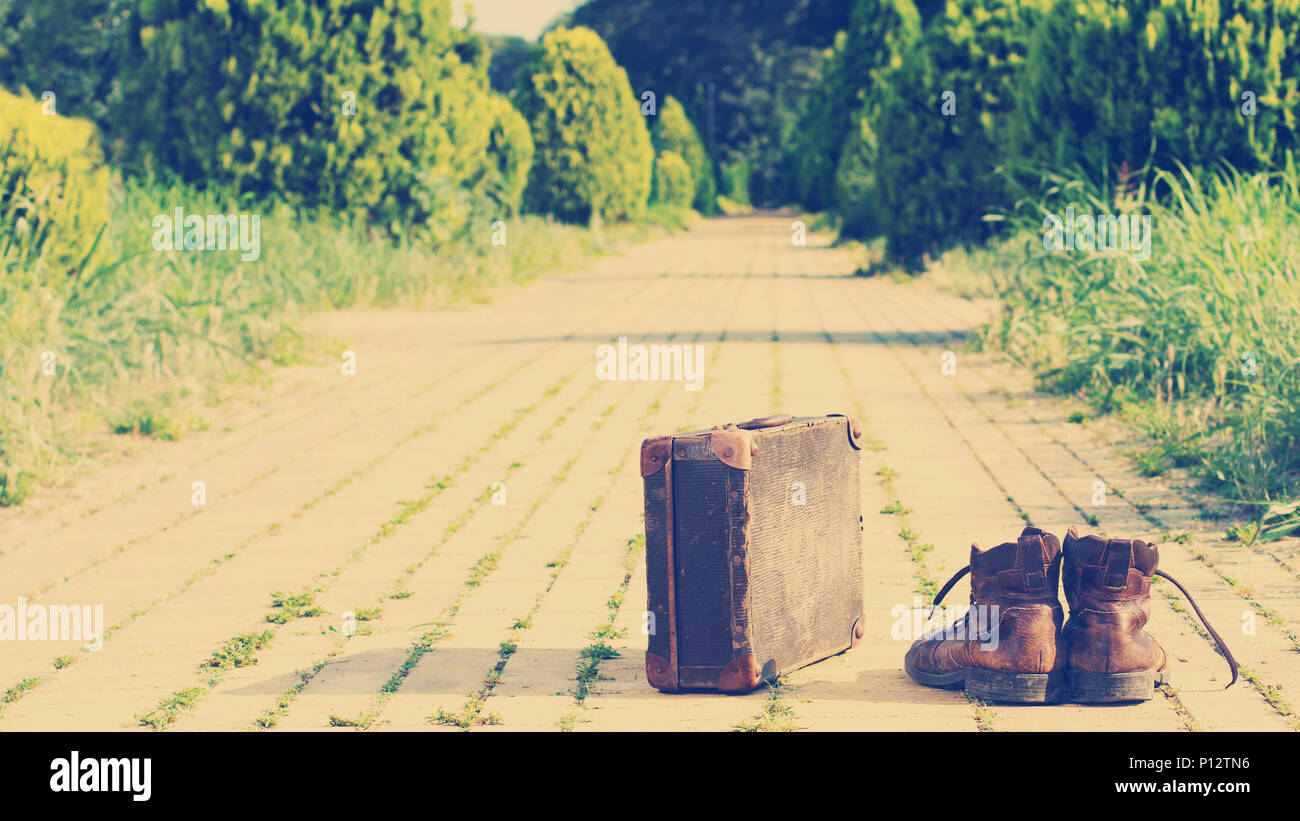 Old shabby leather ankle boots, next to an antique suitcase, in the middle of a yellow brick road. Sixteen-by-Nine crop. Nashville effect added. Stock Photo