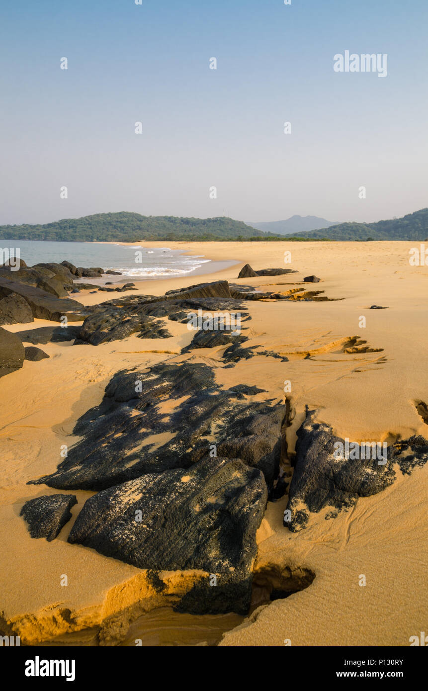 John Obey Beach with black rocks, smooth yellow sand beach, sea and mountains in background, Sierra Leone, Africa Stock Photo