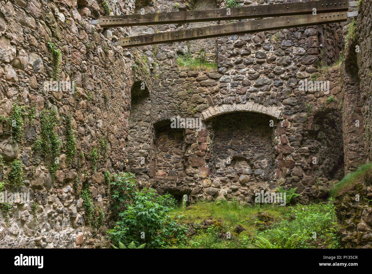 Invergarry, Scotland - June 11, 2012: Tall dark-brown ruined inside walls with wooden studs to support them at castle Invergarry. Weeds have conquered Stock Photo