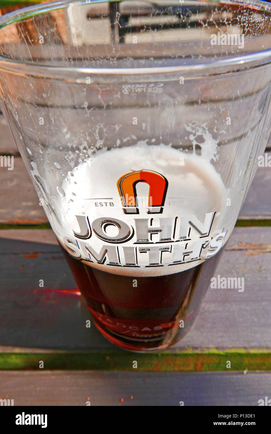 Half full pint of John Smith's bitter sat on a wooden table Stock Photo