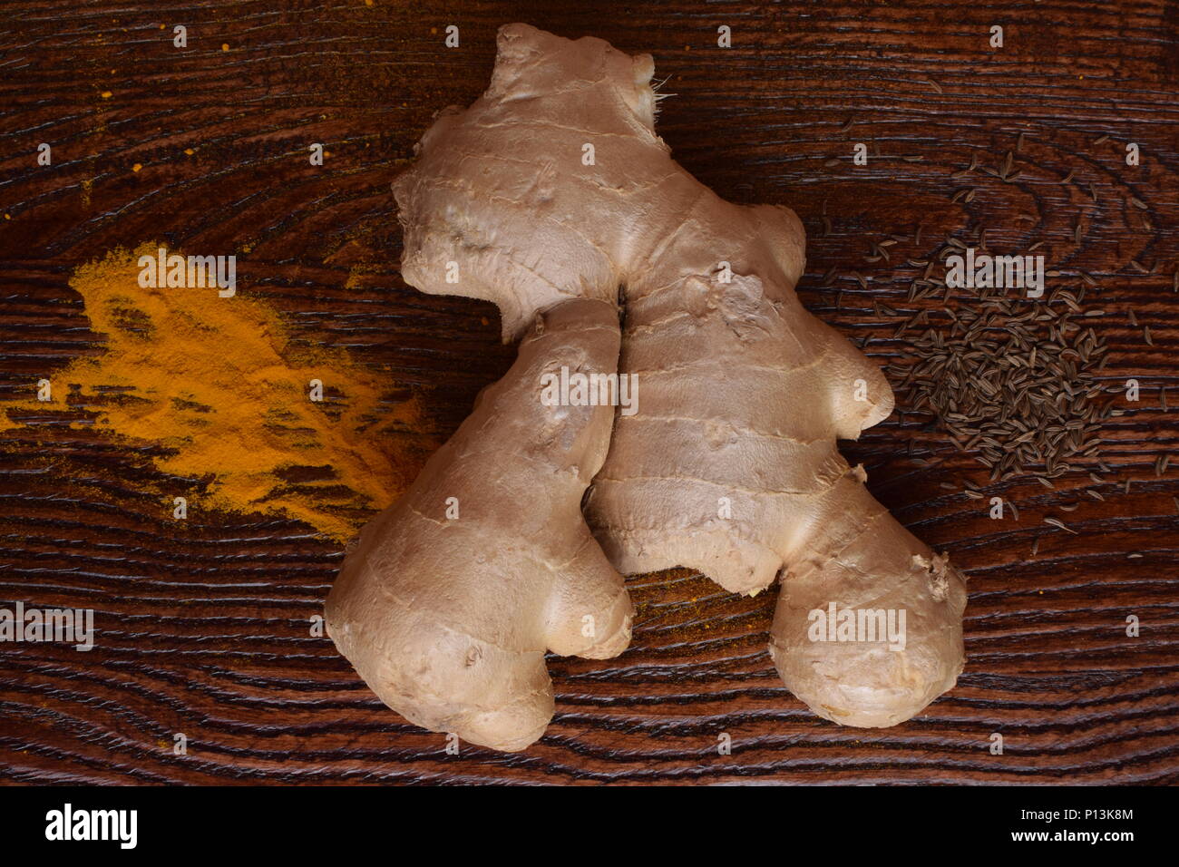 raw ginger root, tumeric powder and black cumin seeds on wooden
