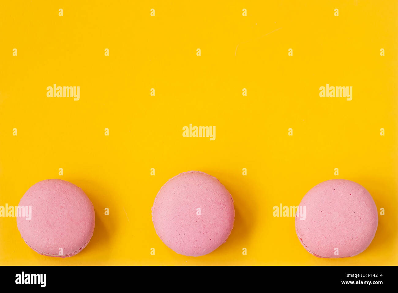 Three macaroons of pink color on yellow background, top view. Romantic morning, gift for beloved. Breakfast on Easter, Valentin's, Mothers, Women's day Stock Photo