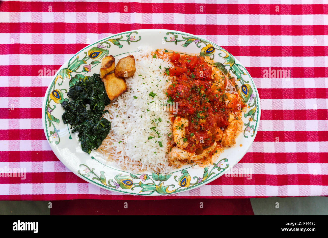 Typical English pub food: a plate of scampi provencale with rice, spinach and fried potatoes, with a red and white gingham checked tablecloth backgrou Stock Photo