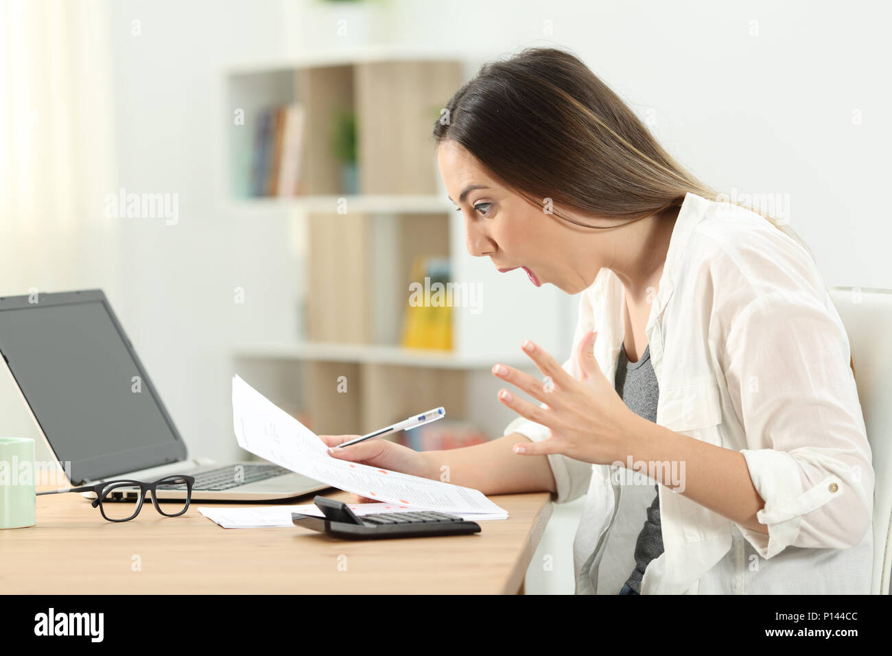 Side view portrait of a surprised woman reading bank statements at home Stock Photo