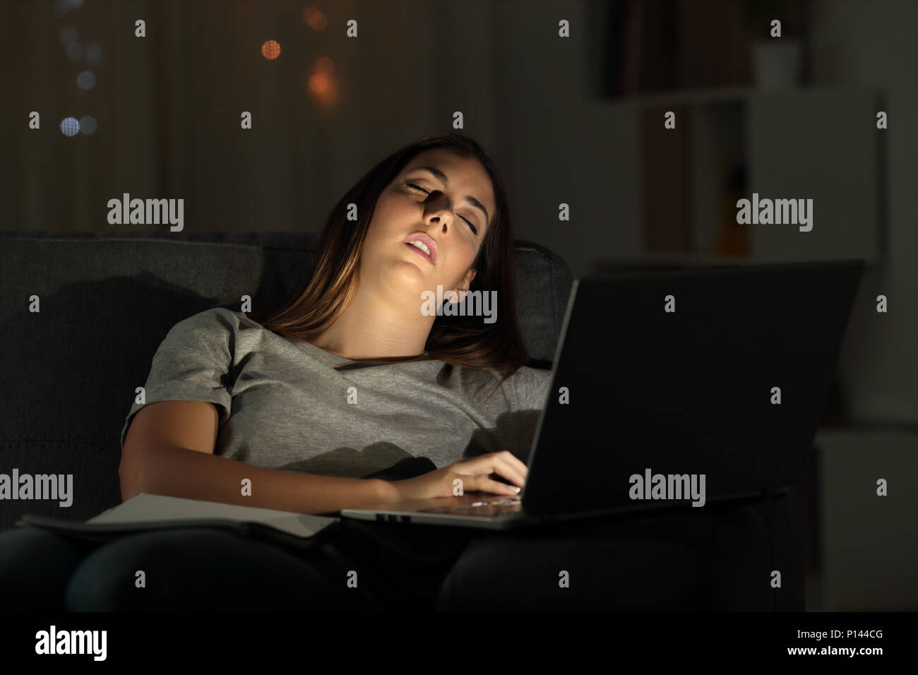 Tired woman sleeping on a couch beside a laptop in the night at home