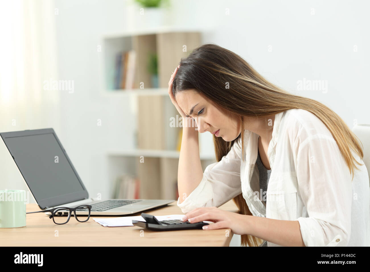 Worried housewife doing accounting using a calculator at home Stock Photo