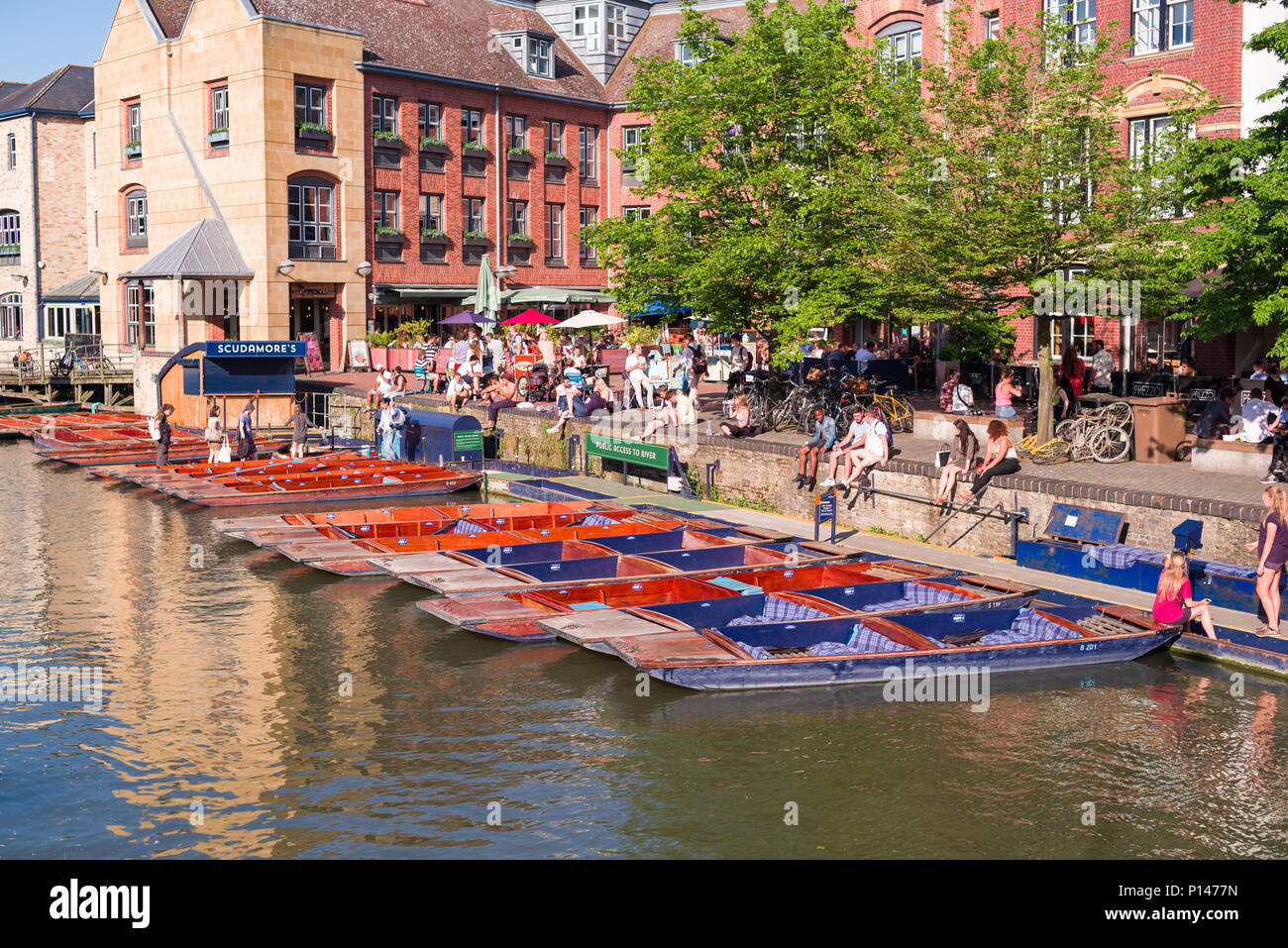 People sit outside by the river Cam with punt boats moored up on a sunny Summer afternoon, Cambridge, UK Stock Photo