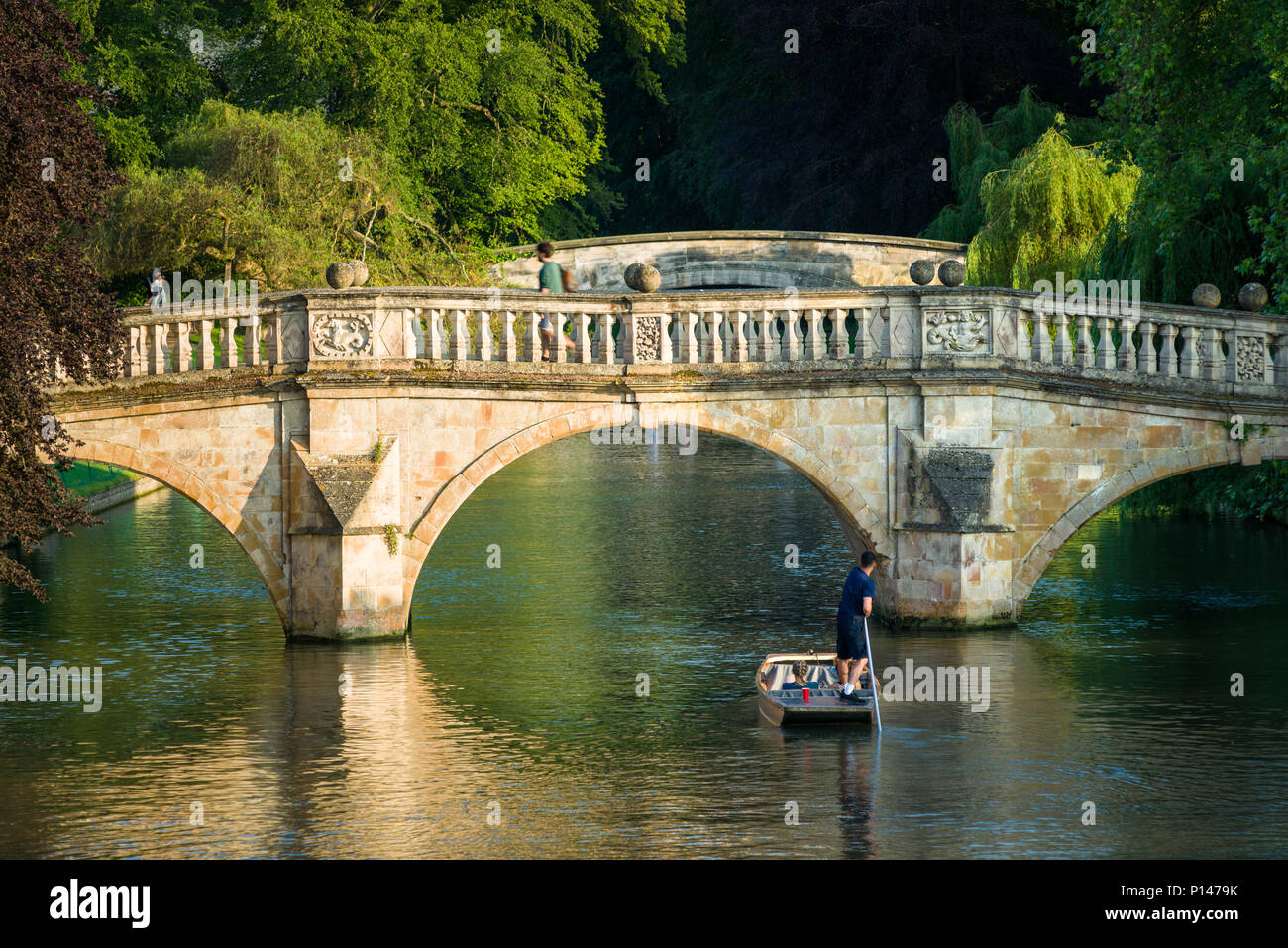 A man steers a punt boat with a couple in towards a stone bridge near Clares college, Cambridge, UK Stock Photo