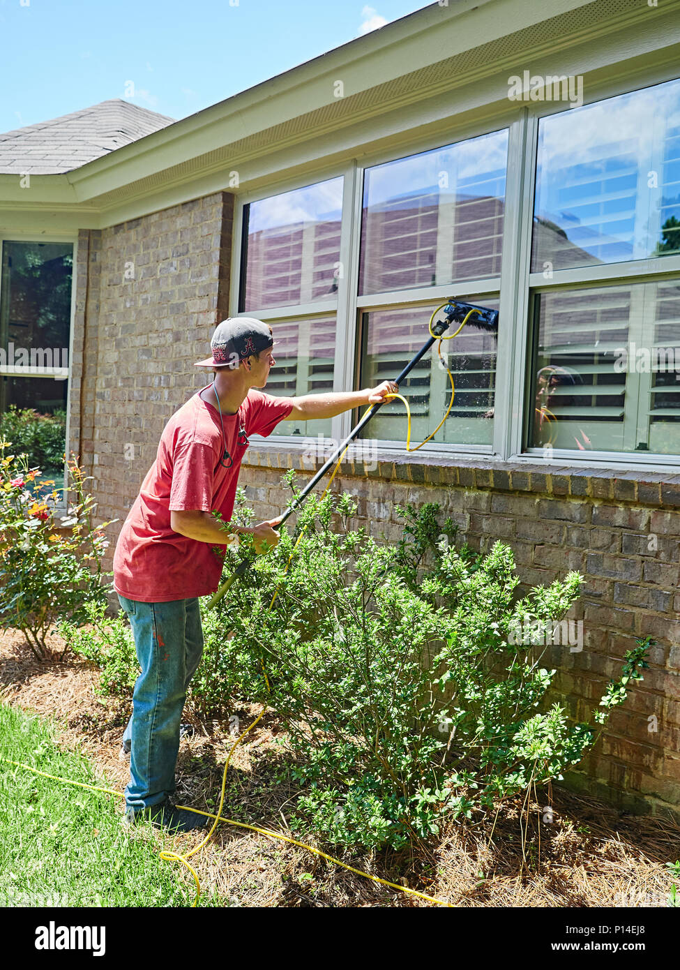 White male adult window washer employee or worker washing windows on a residential house or home in suburban America. Stock Photo