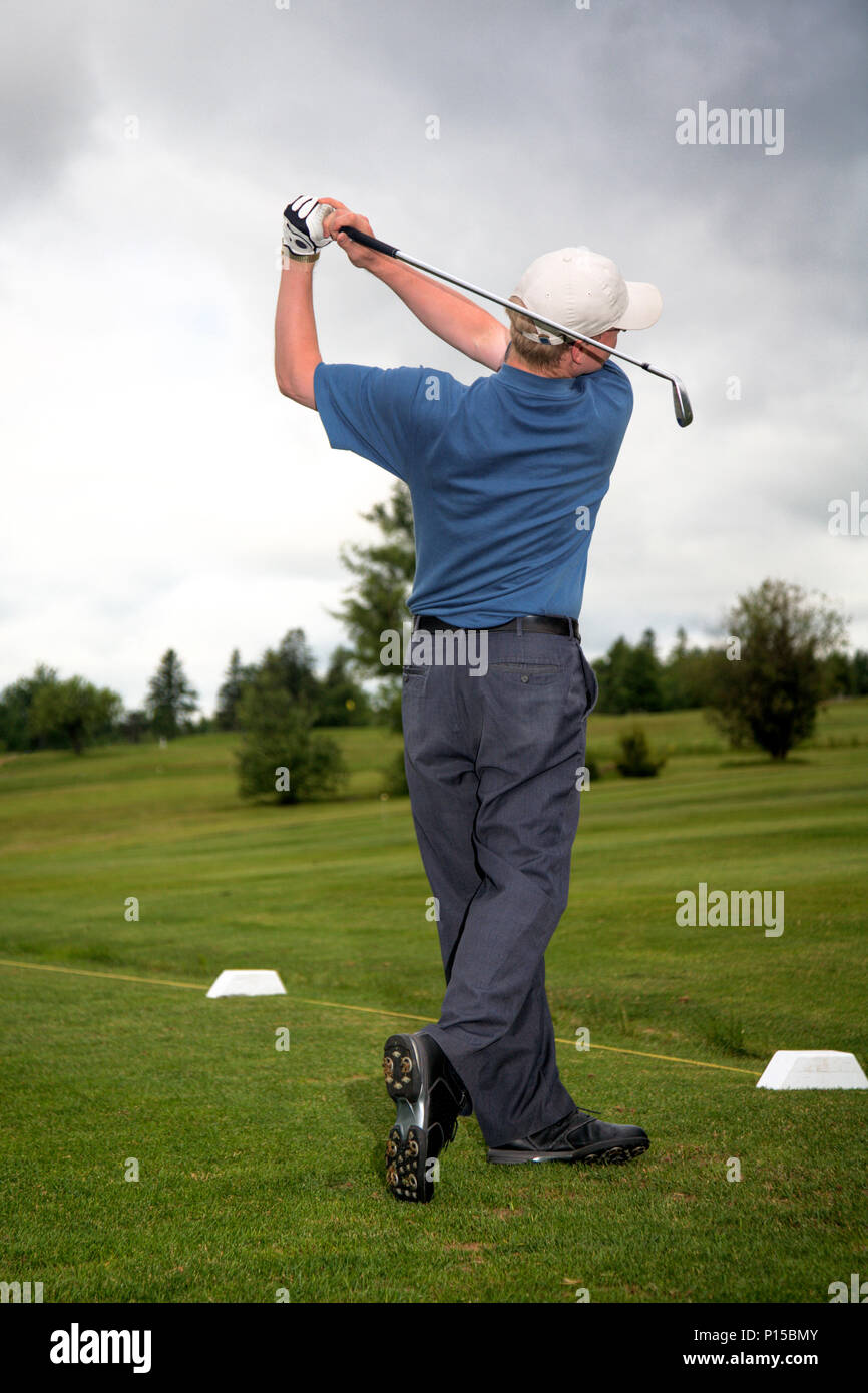 A man practices his golf swing on a green fairway on a cloudy day. Stock Photo