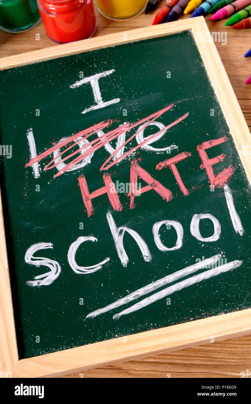 The words I Hate School written on a small elementary blackboard with various paints, crayons and pencils on a school desk. Stock Photo