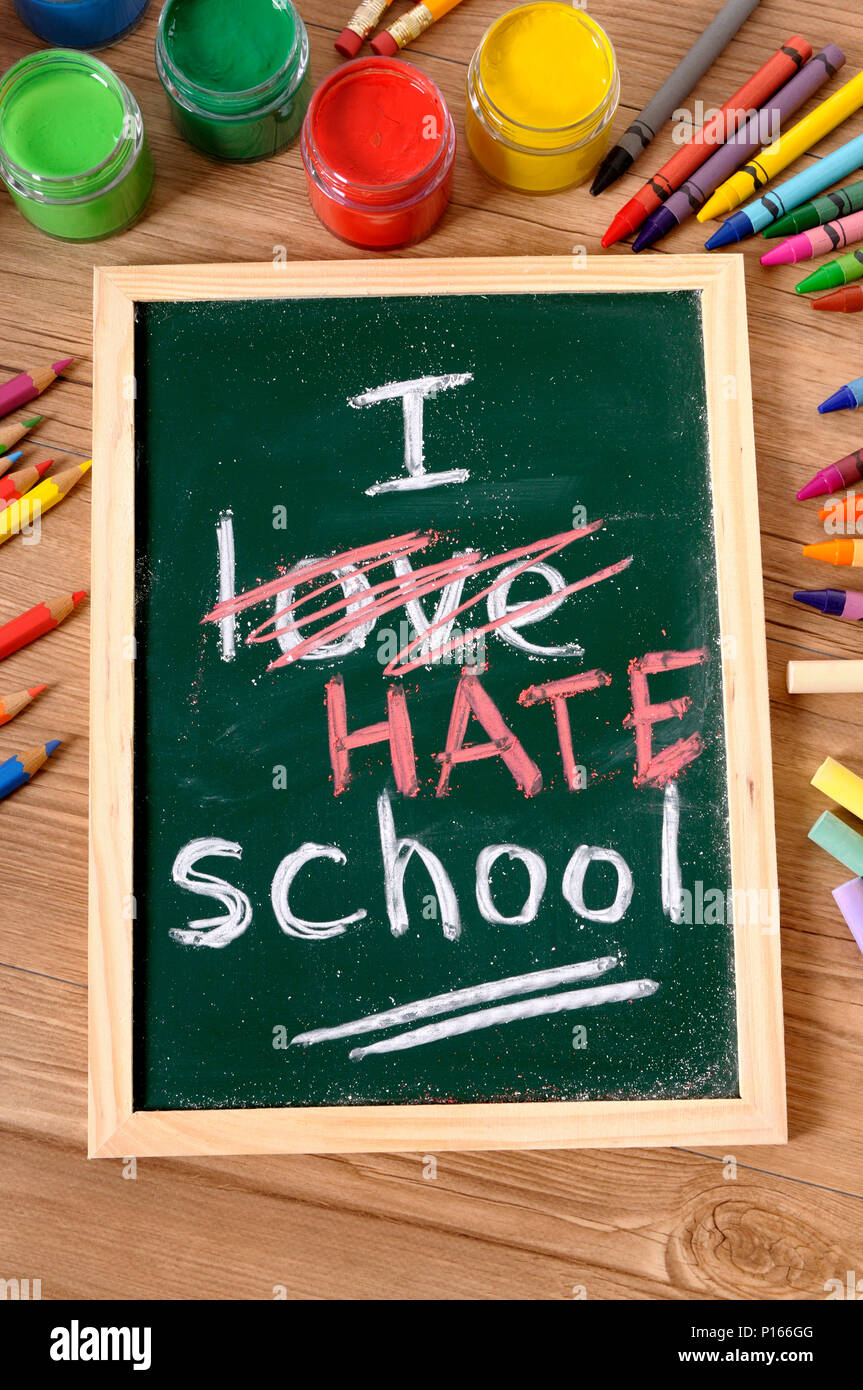 The words I Hate School written on a small elementary blackboard with various paints, crayons and pencils on a school desk. Stock Photo